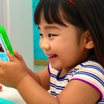 **A young Thai child happily interacting with the Cocomelon app on a mobile phone. The scene is safe and educational, emphasizing colorful visuals and learning.**